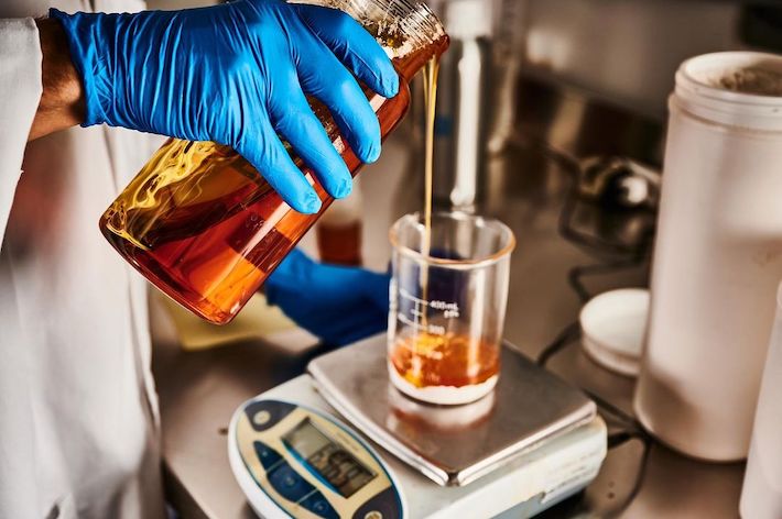 Pouring delta-8 distillate oil in a large glass jar at a lab